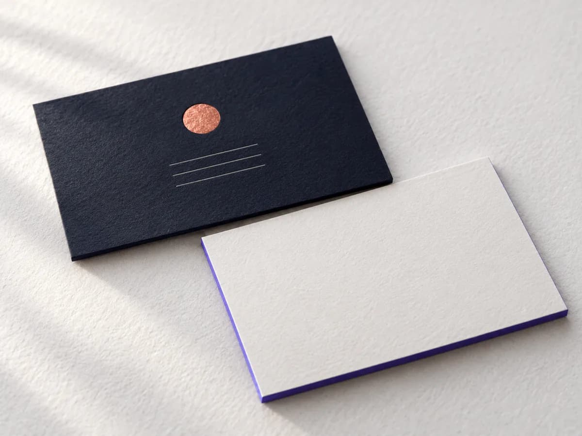Illustration of 2 Australian business cards on textured paper, 1 navy with a copper foil circle and 1 off-white with a violet painted edge